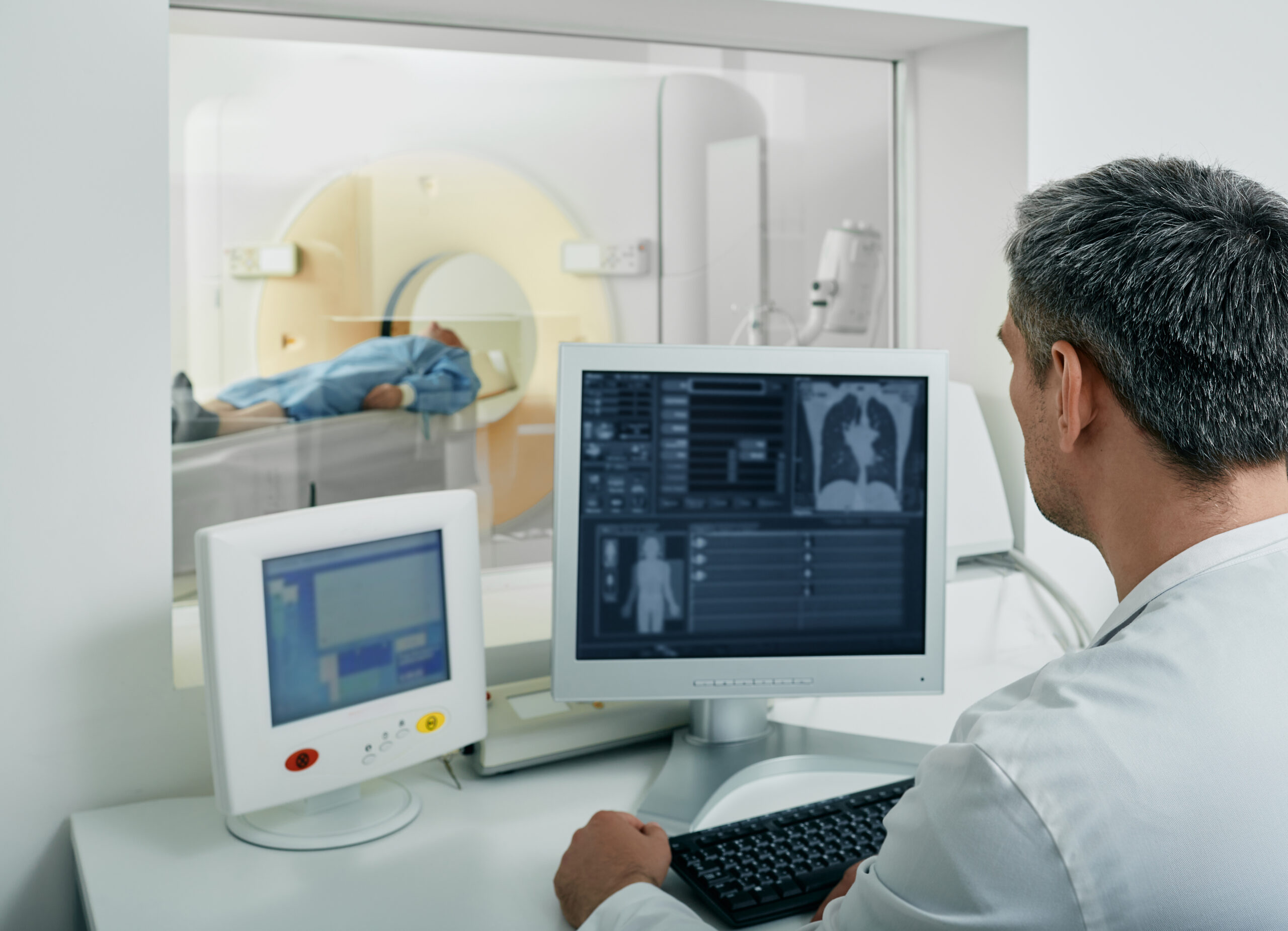 Technologist running CT scan for patient's body lungs from control room. Computed Tomography